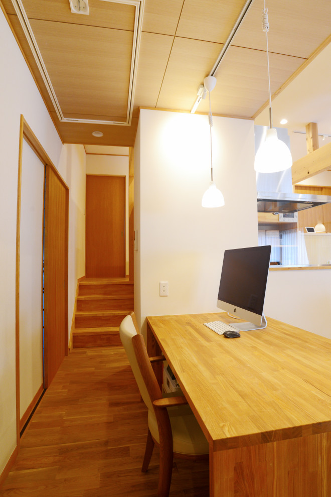 This is an example of a medium sized world-inspired study in Other with white walls, light hardwood flooring, a built-in desk, beige floors, a wood ceiling and wallpapered walls.