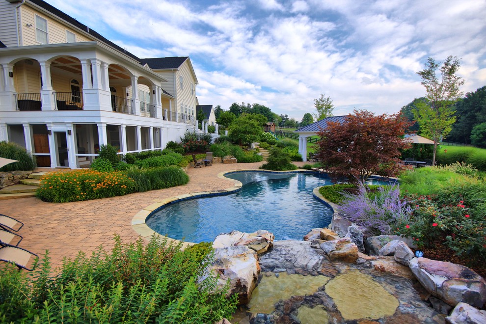 Photo of a large traditional backyard custom-shaped pool in DC Metro with a water feature and brick pavers.