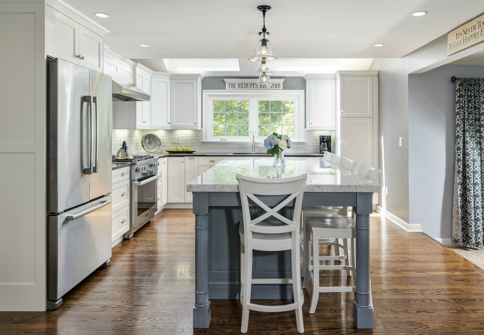 Inspiration for a mid-sized transitional l-shaped medium tone wood floor eat-in kitchen remodel with a single-bowl sink, recessed-panel cabinets, white cabinets, granite countertops, white backsplash, ceramic backsplash, stainless steel appliances and an island