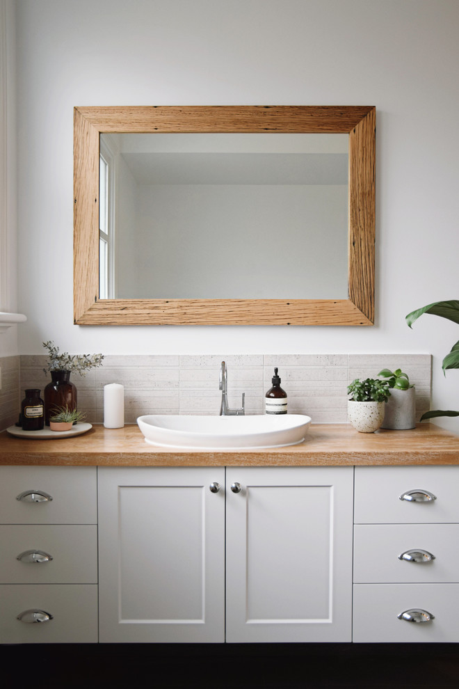 This is an example of a large traditional bathroom in Melbourne with white cabinets, wood benchtops, gray tile, ceramic tile, white walls, a drop-in sink, flat-panel cabinets and brown benchtops.
