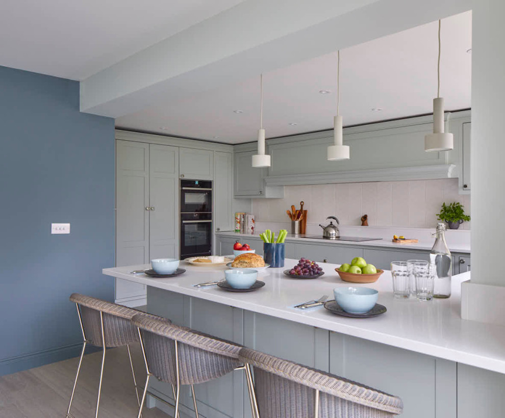 Inspiration for a contemporary u-shaped eat-in kitchen in Gloucestershire with an integrated sink, shaker cabinets, green cabinets, quartzite benchtops, white splashback, ceramic splashback, black appliances, vinyl floors, a peninsula, grey floor and white benchtop.