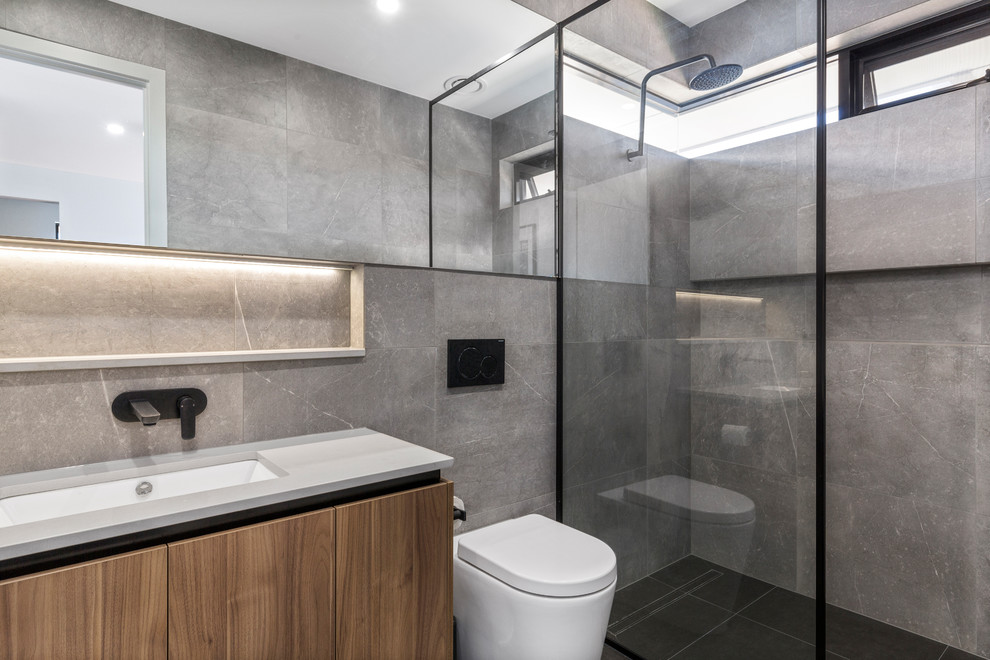 Inspiration for a contemporary 3/4 bathroom in Adelaide with flat-panel cabinets, medium wood cabinets, an open shower, a wall-mount toilet, gray tile, grey walls, an undermount sink, black floor, an open shower and grey benchtops.