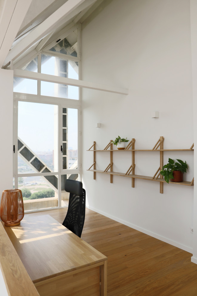 Immagine di un grande atelier moderno con pareti bianche, pavimento in legno massello medio, scrivania autoportante e travi a vista