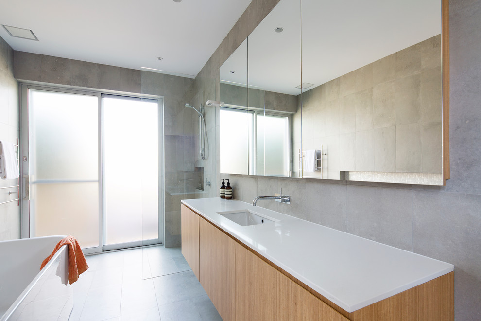 Photo of a large contemporary kids bathroom in Sydney with light wood cabinets, a freestanding tub, a curbless shower, gray tile, porcelain tile, grey walls, ceramic floors, an undermount sink and solid surface benchtops.