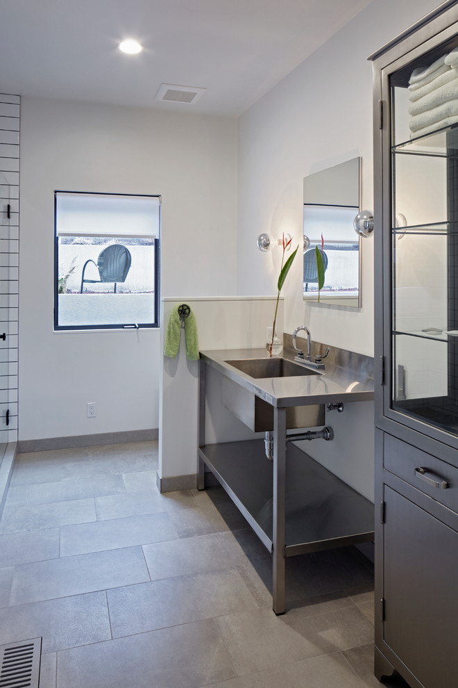 This is an example of a contemporary 3/4 bathroom in Portland with open cabinets, a corner shower, white tile, subway tile, white walls, porcelain floors, an integrated sink, stainless steel benchtops, grey floor, a hinged shower door and grey benchtops.