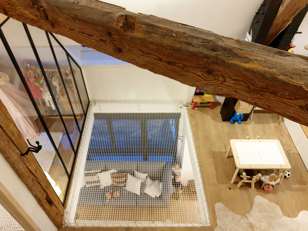 This is an example of a mid-sized modern gender-neutral kids' playroom for kids 4-10 years old with white walls, light hardwood floors and exposed beam.