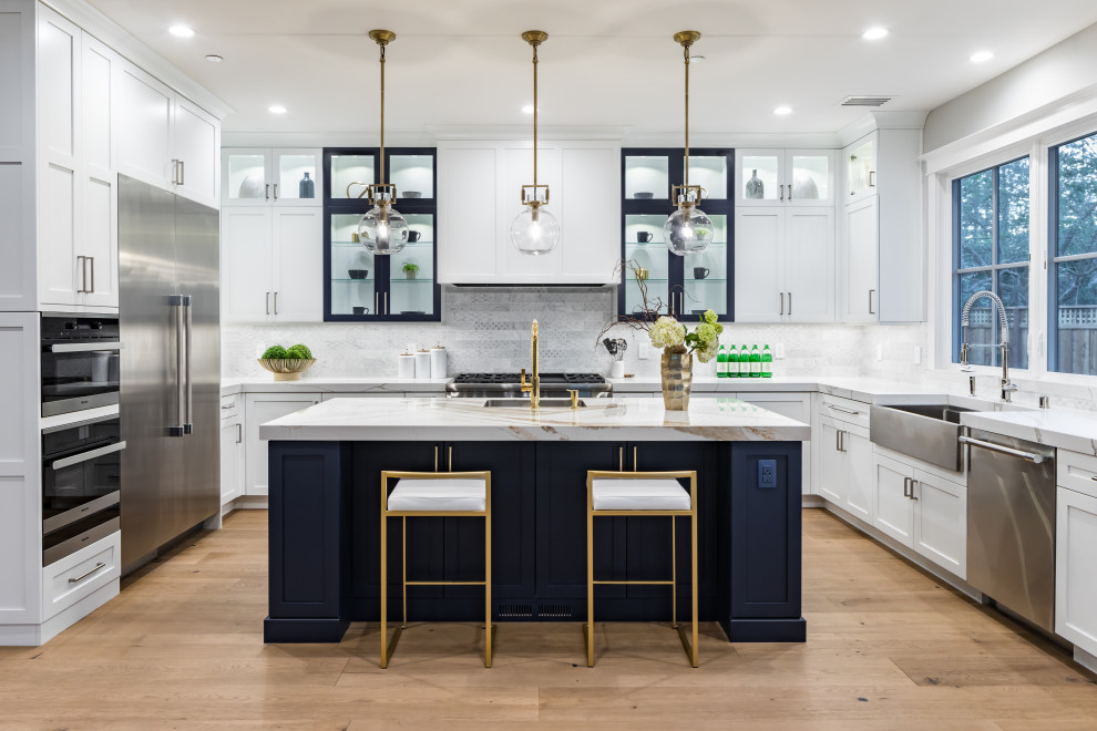 Inspiration for a transitional u-shaped kitchen in San Francisco with a farmhouse sink, shaker cabinets, white cabinets, white splashback, stainless steel appliances, light hardwood floors, with island, beige floor and white benchtop.