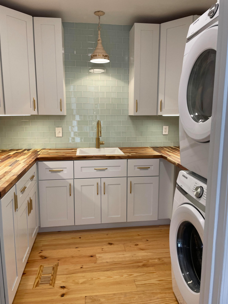 Photo of a mid-sized country laundry room in Charlotte with a drop-in sink, wood benchtops, glass tile splashback and light hardwood floors.