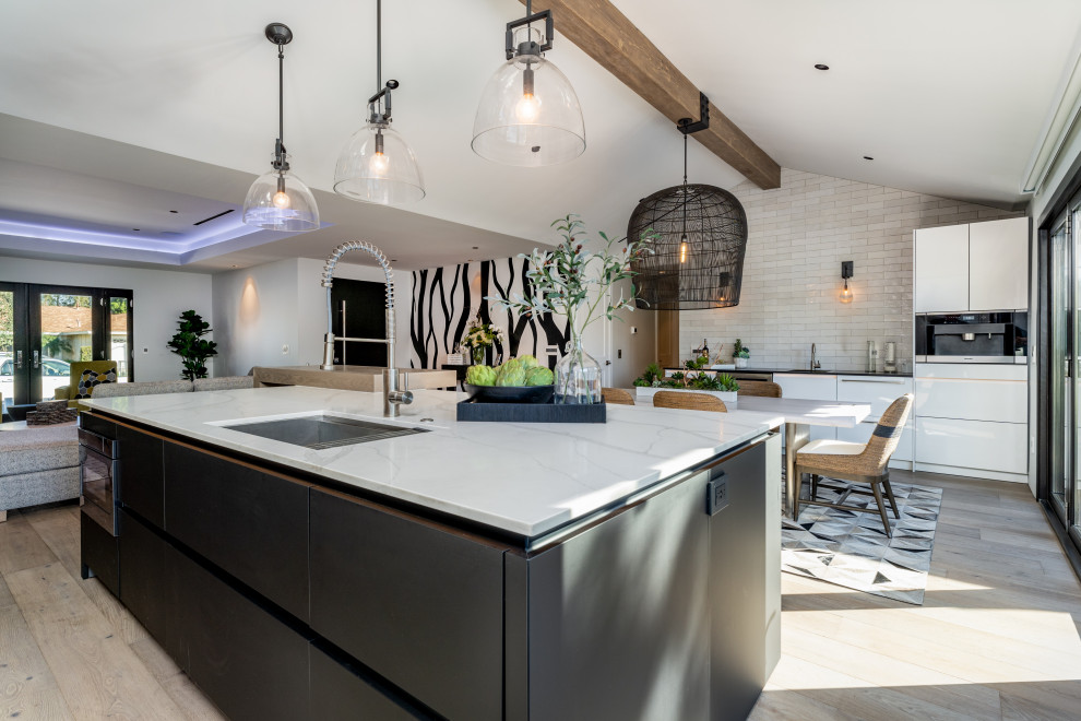 Inspiration for a mid-sized modern eat-in kitchen in Orange County with an undermount sink, flat-panel cabinets, black cabinets, quartz benchtops, white splashback, porcelain splashback, stainless steel appliances, light hardwood floors, with island, beige floor, white benchtop and vaulted.