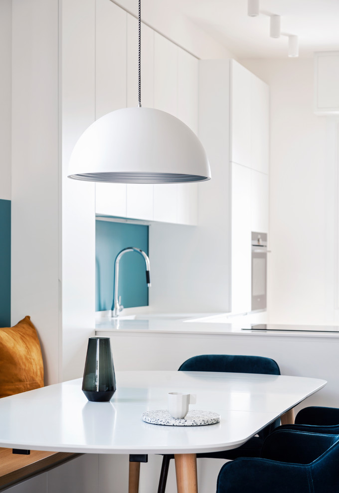 Mid-sized contemporary l-shaped open plan kitchen in Milan with an integrated sink, flat-panel cabinets, white cabinets, solid surface benchtops, blue splashback, black appliances, medium hardwood floors, a peninsula and white benchtop.
