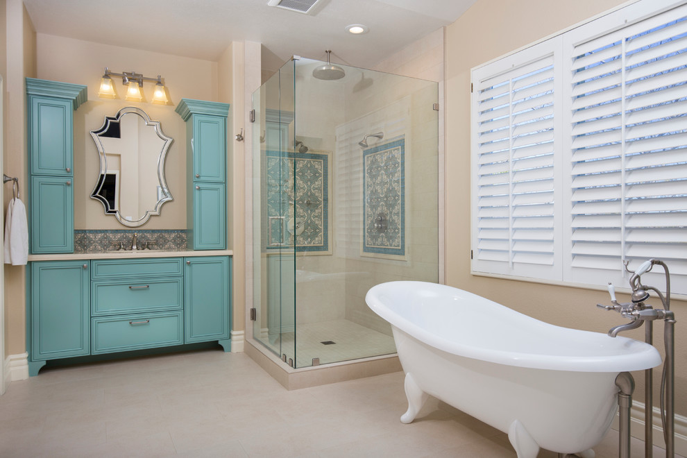 Photo of a large mediterranean master bathroom in San Diego with recessed-panel cabinets, blue cabinets, a corner shower, a one-piece toilet, beige tile, porcelain tile, beige walls, porcelain floors, an undermount sink, engineered quartz benchtops and a claw-foot tub.
