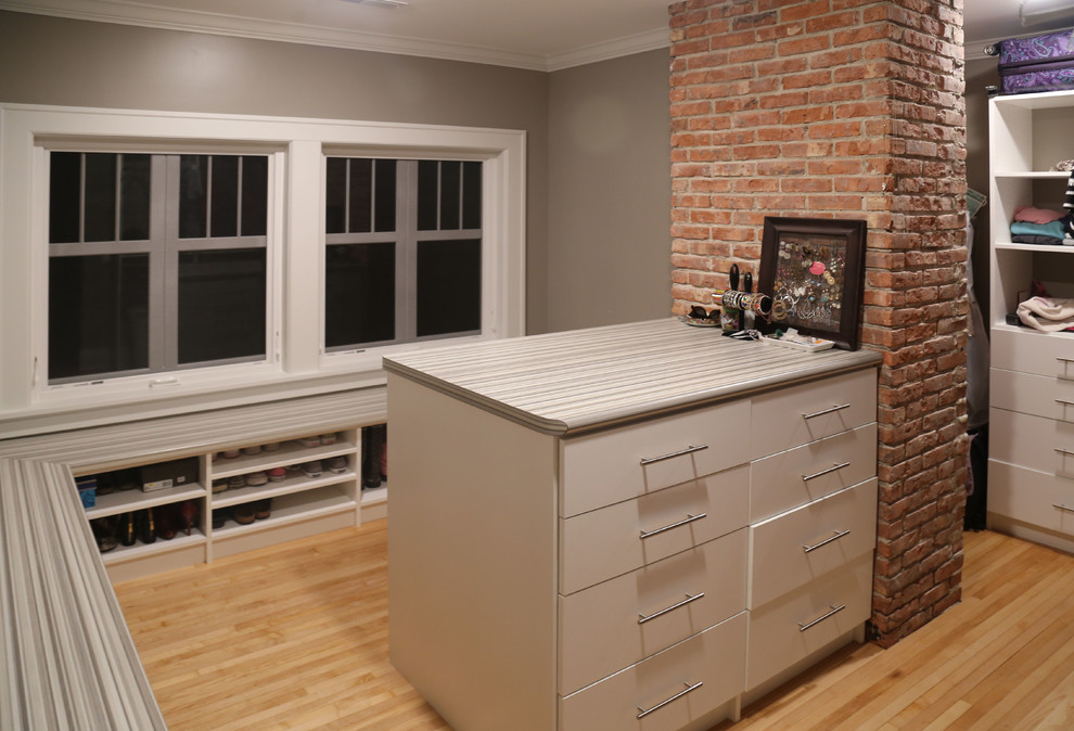 Example of a mid-sized transitional gender-neutral light wood floor walk-in closet design with flat-panel cabinets and white cabinets