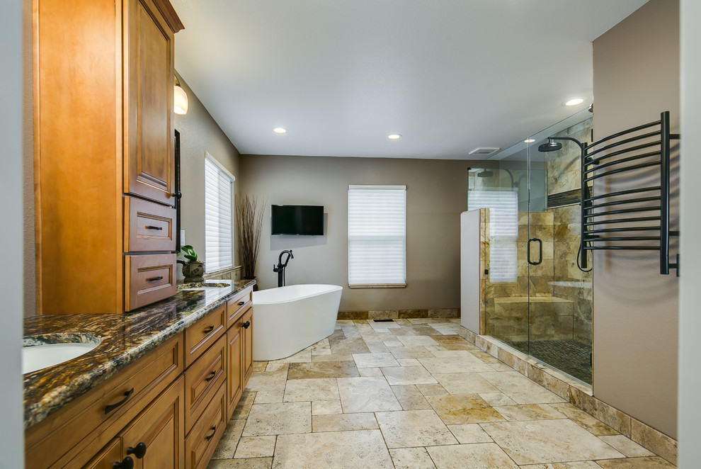Large traditional master bathroom in Denver with medium wood cabinets, a freestanding tub, a double shower, a one-piece toilet, beige tile, travertine, beige walls, travertine floors, an undermount sink, granite benchtops, recessed-panel cabinets, beige floor and a hinged shower door.