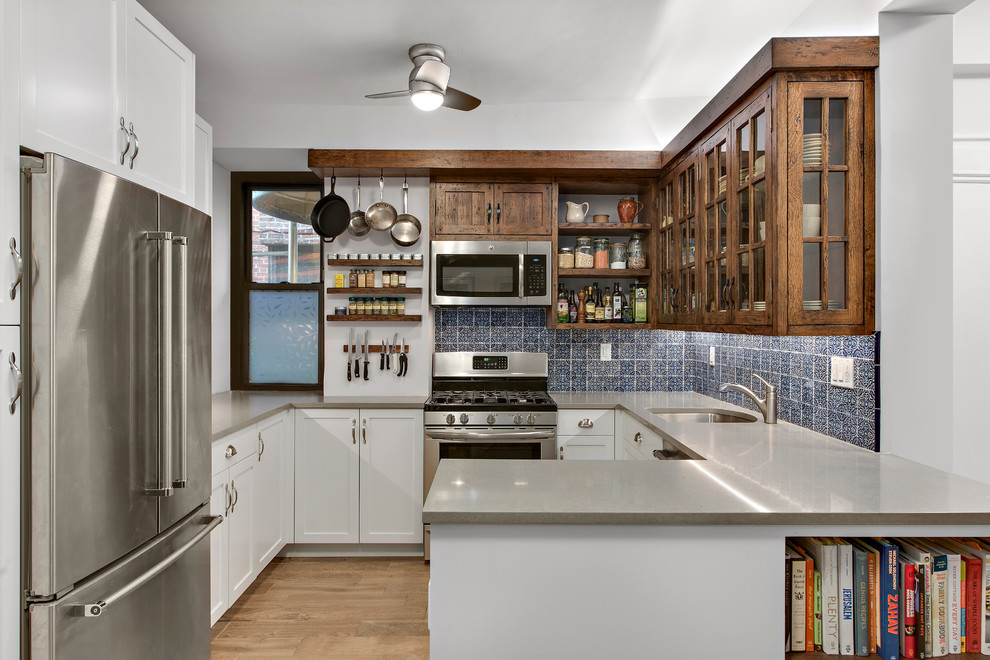 Transitional u-shaped medium tone wood floor and brown floor kitchen photo in New York with an undermount sink, shaker cabinets, white cabinets, blue backsplash, stainless steel appliances, a peninsula and gray countertops