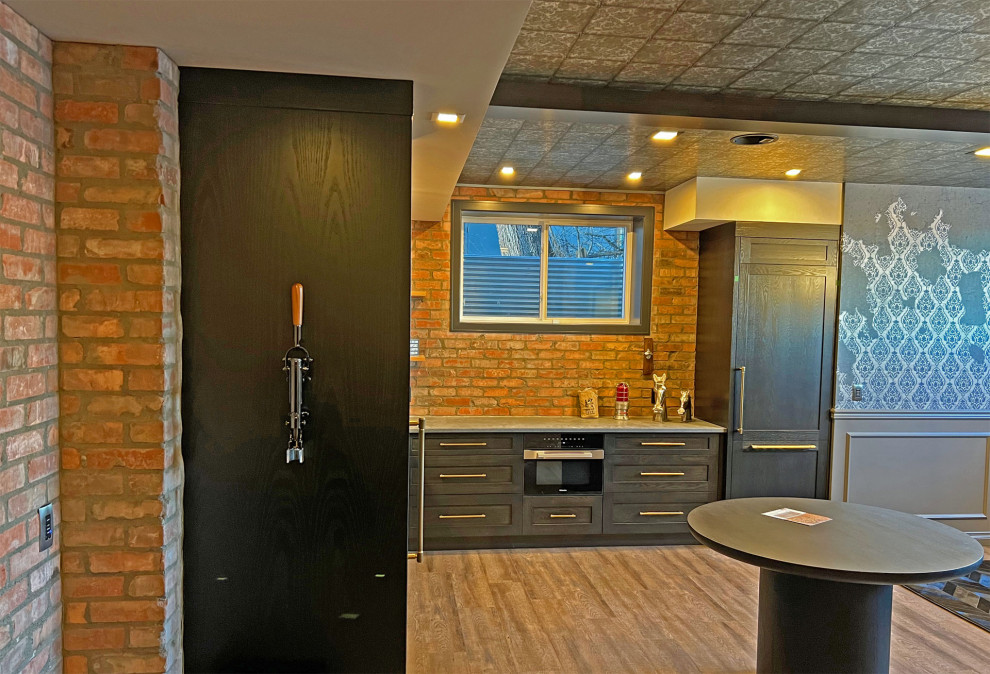 Design ideas for a large eclectic l-shaped wet bar in Calgary with an integrated sink, recessed-panel cabinets, black cabinets, granite benchtops, brick splashback, medium hardwood floors, brown floor and grey benchtop.
