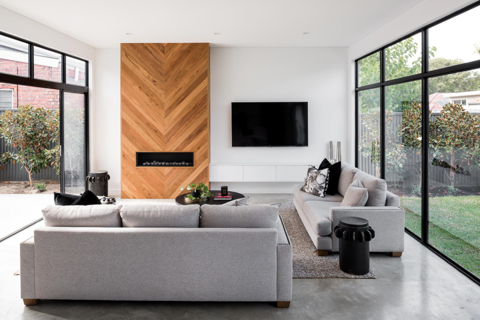 Immagine di un piccolo soggiorno minimalista aperto con pavimento in cemento, camino classico, cornice del camino in legno, TV a parete e pavimento grigio