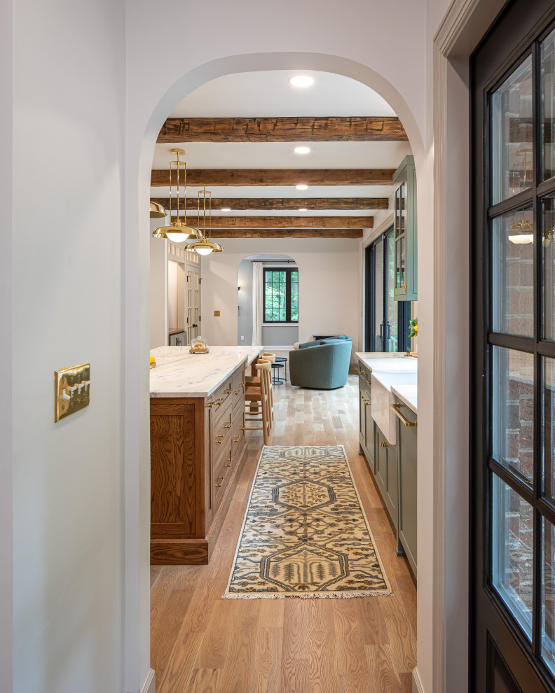Photo of a large traditional galley open plan kitchen in Raleigh with a farmhouse sink, shaker cabinets, green cabinets, quartzite benchtops, green splashback, cement tile splashback, stainless steel appliances, medium hardwood floors, with island, brown floor, white benchtop and exposed beam.