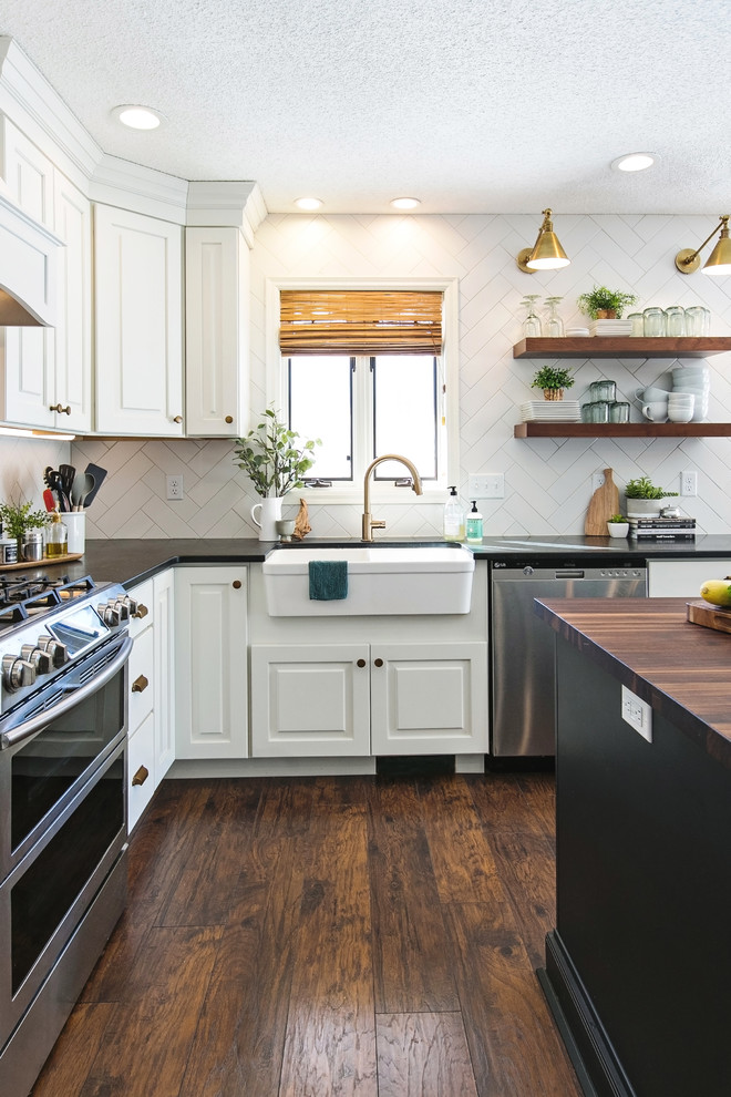 Photo of a large eclectic l-shaped open plan kitchen in Atlanta with a farmhouse sink, shaker cabinets, white cabinets, wood benchtops, white splashback, porcelain splashback, stainless steel appliances, dark hardwood floors, with island, brown floor and brown benchtop.