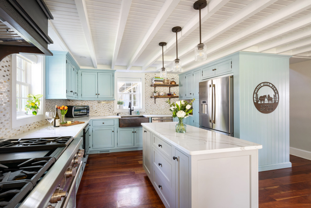 Foto på ett avskilt, mellanstort lantligt vit kök, med en rustik diskho, luckor med infälld panel, blå skåp, bänkskiva i kvarts, flerfärgad stänkskydd, stänkskydd i mosaik, rostfria vitvaror, mellanmörkt trägolv, en köksö och brunt golv