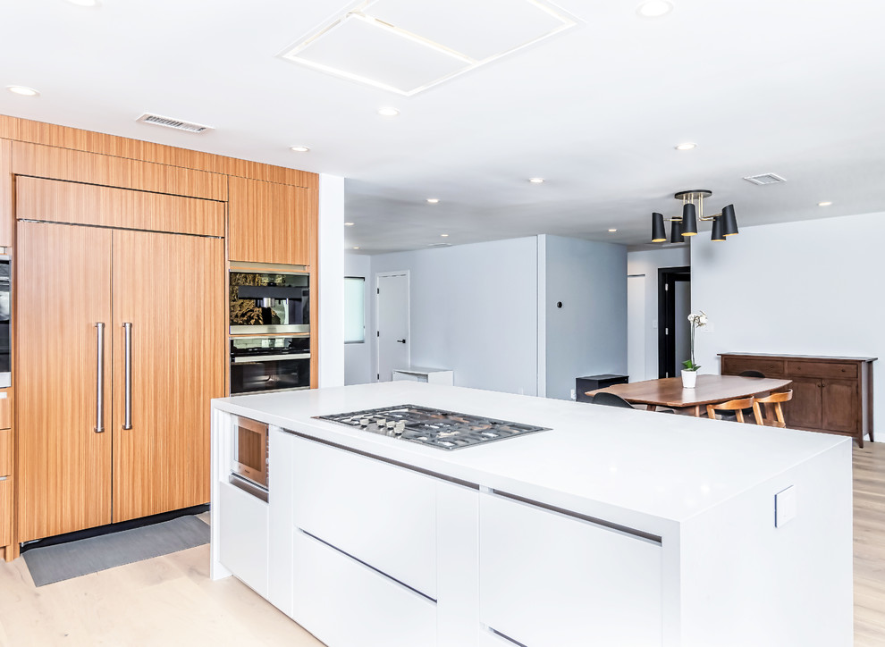 This is an example of a mid-sized contemporary u-shaped eat-in kitchen in Los Angeles with a drop-in sink, flat-panel cabinets, white cabinets, quartz benchtops, stainless steel appliances, light hardwood floors, with island, beige floor and white benchtop.