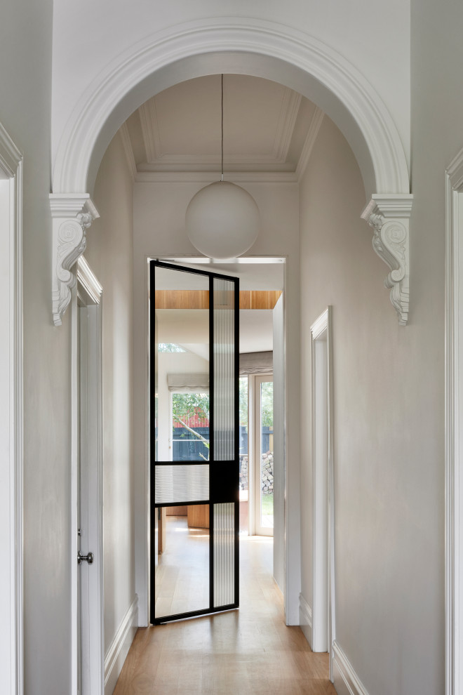 Cette photo montre un petit couloir tendance avec un mur blanc, parquet clair et un sol marron.