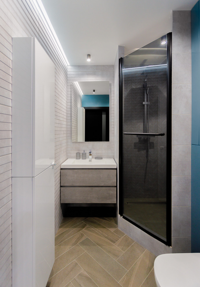 На фото: серо-белая ванная комната среднего размера: освещение в современном стиле с плоскими фасадами, серыми фасадами, душевой комнатой, раздельным унитазом, белой плиткой, плиткой из листового камня, белыми стенами, полом из ламината, душевой кабиной, консольной раковиной, столешницей из искусственного камня, бежевым полом, душем с распашными дверями, белой столешницей, тумбой под одну раковину, подвесной тумбой, многоуровневым потолком и панелями на части стены с