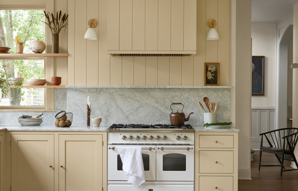 Bild på ett mellanstort vintage grå grått kök och matrum, med skåp i shakerstil, gula skåp, marmorbänkskiva, grått stänkskydd, stänkskydd i marmor, vita vitvaror, mellanmörkt trägolv och brunt golv