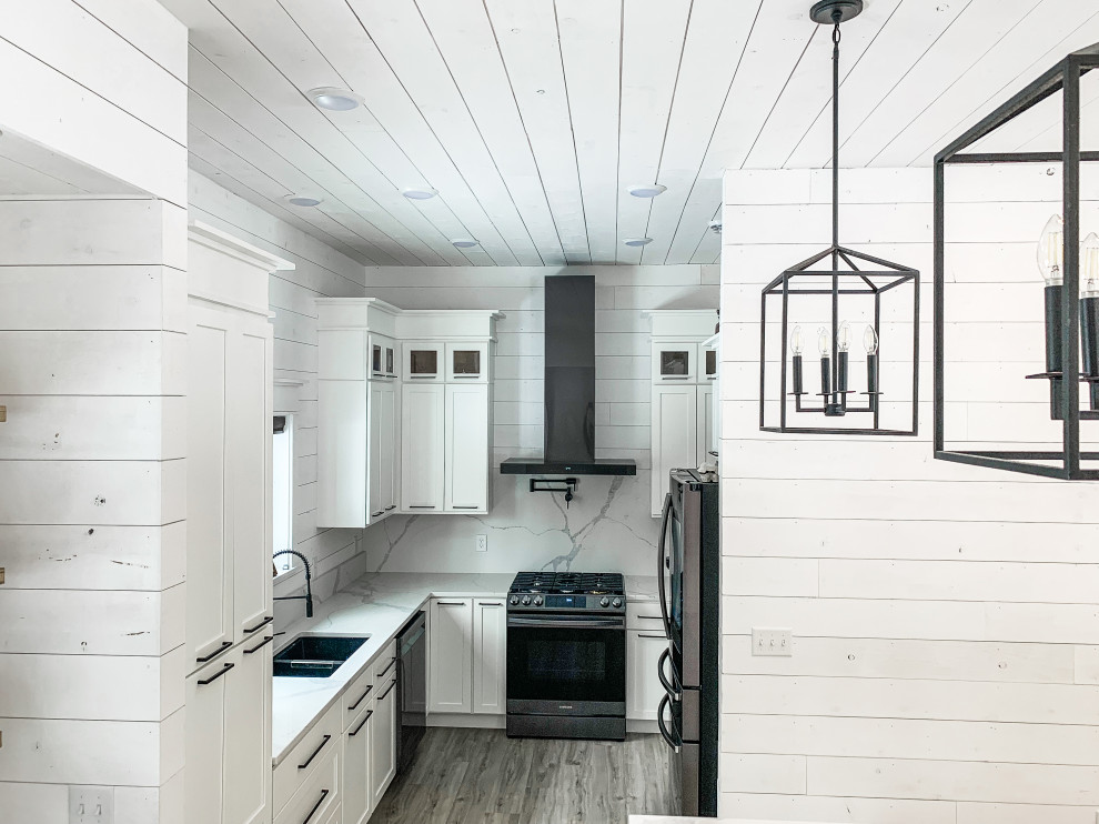 Exempel på ett stort lantligt vit vitt kök, med en undermonterad diskho, skåp i shakerstil, vita skåp, bänkskiva i kvartsit, vitt stänkskydd, svarta vitvaror, laminatgolv, en köksö och brunt golv