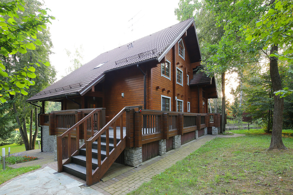 This is an example of a large country three-storey brown house exterior in Moscow with wood siding, a gable roof and a tile roof.