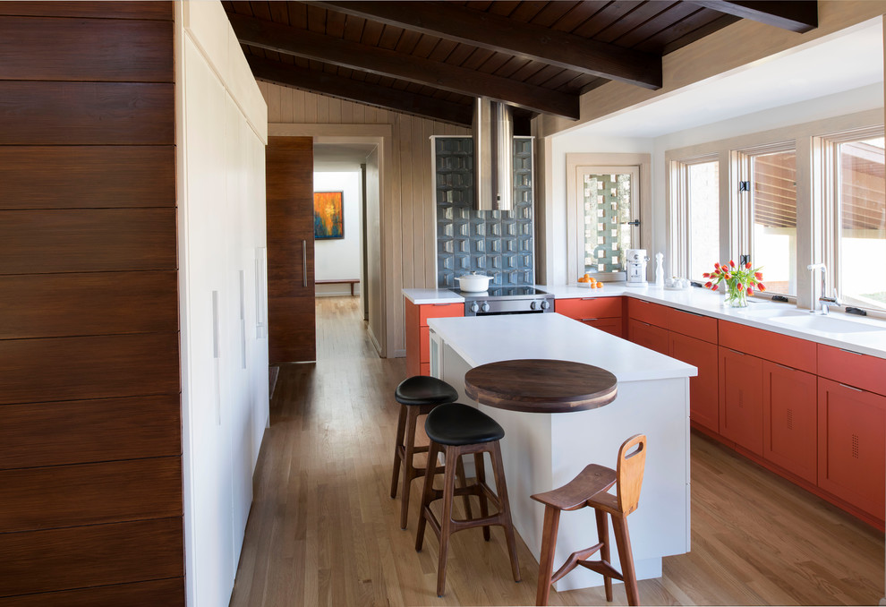 Mid-sized midcentury l-shaped eat-in kitchen in Atlanta with a double-bowl sink, shaker cabinets, orange cabinets, solid surface benchtops, stainless steel appliances, light hardwood floors and with island.
