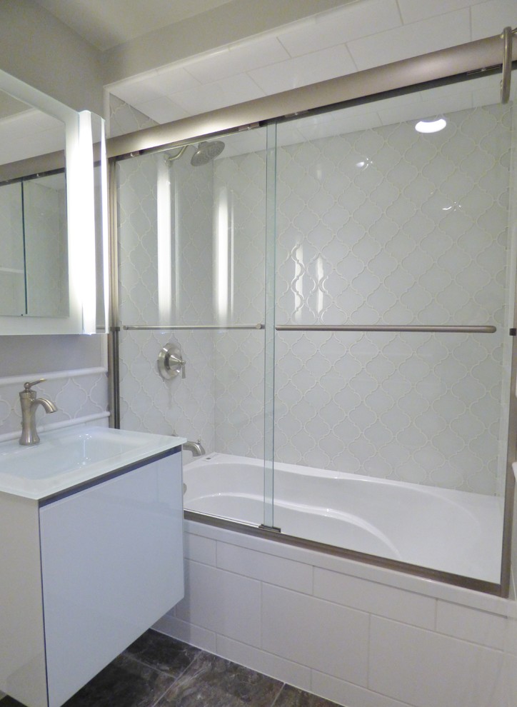 This is an example of a small traditional master bathroom in Other with flat-panel cabinets, white cabinets, a drop-in tub, a shower/bathtub combo, a one-piece toilet, gray tile, glass tile, beige walls, porcelain floors, a drop-in sink, glass benchtops, multi-coloured floor and a sliding shower screen.