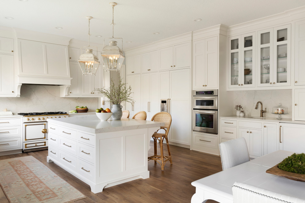 Bild på ett mycket stort vintage vit vitt kök, med en rustik diskho, luckor med infälld panel, vita skåp, bänkskiva i kvarts, vitt stänkskydd, vita vitvaror, ljust trägolv, en köksö och brunt golv