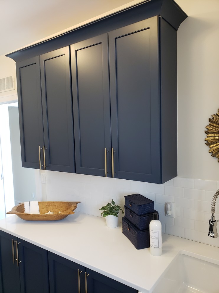 Small arts and crafts galley dedicated laundry room in Detroit with a farmhouse sink, recessed-panel cabinets, blue cabinets, quartzite benchtops, beige walls, ceramic floors, a side-by-side washer and dryer, grey floor and white benchtop.