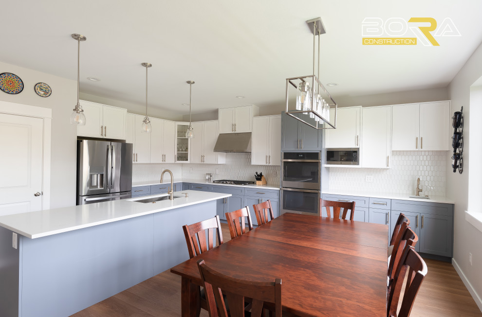 Example of a large transitional l-shaped medium tone wood floor and brown floor eat-in kitchen design in Seattle with an undermount sink, shaker cabinets, blue cabinets, quartz countertops, white backsplash, ceramic backsplash, stainless steel appliances, an island and white countertops