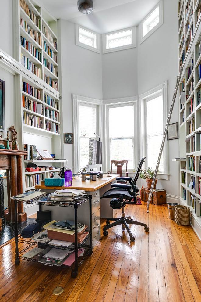 Ejemplo de despacho clásico de tamaño medio con biblioteca, paredes blancas, suelo de madera en tonos medios, todas las chimeneas, marco de chimenea de madera, escritorio independiente y suelo marrón