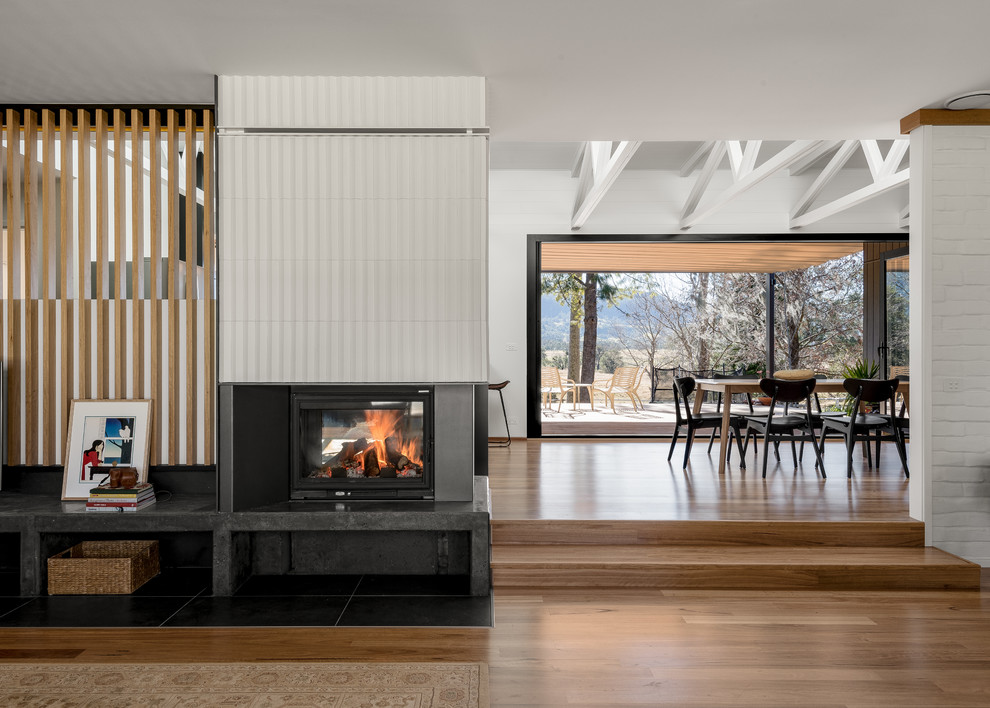 Large midcentury open concept living room in Other with white walls, medium hardwood floors, a two-sided fireplace and a tile fireplace surround.