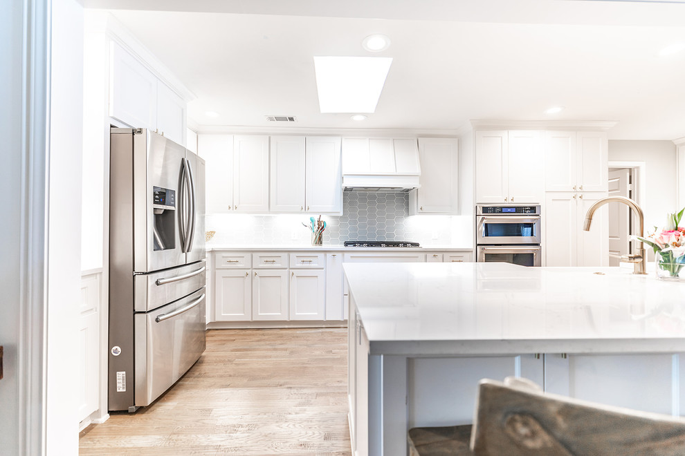 Transitional eat-in kitchen in Dallas with a farmhouse sink, shaker cabinets, white cabinets, quartz benchtops, blue splashback, ceramic splashback, stainless steel appliances, light hardwood floors, with island and white benchtop.