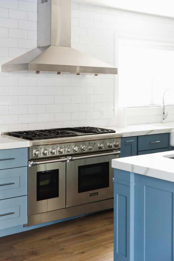 Inspiration for a large transitional l-shaped kitchen in Boston with a farmhouse sink, shaker cabinets, blue cabinets, quartzite benchtops, white splashback, subway tile splashback, stainless steel appliances, medium hardwood floors and with island.