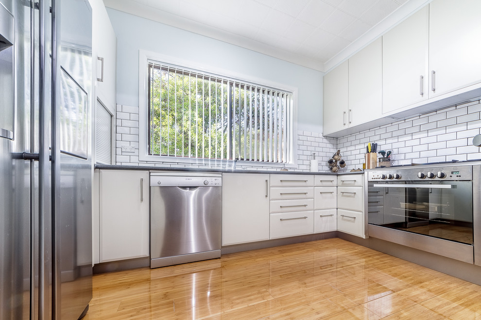 Inspiration for a small contemporary u-shaped separate kitchen in Canberra - Queanbeyan with a single-bowl sink, flat-panel cabinets, beige cabinets, laminate benchtops, white splashback, subway tile splashback, stainless steel appliances and bamboo floors.