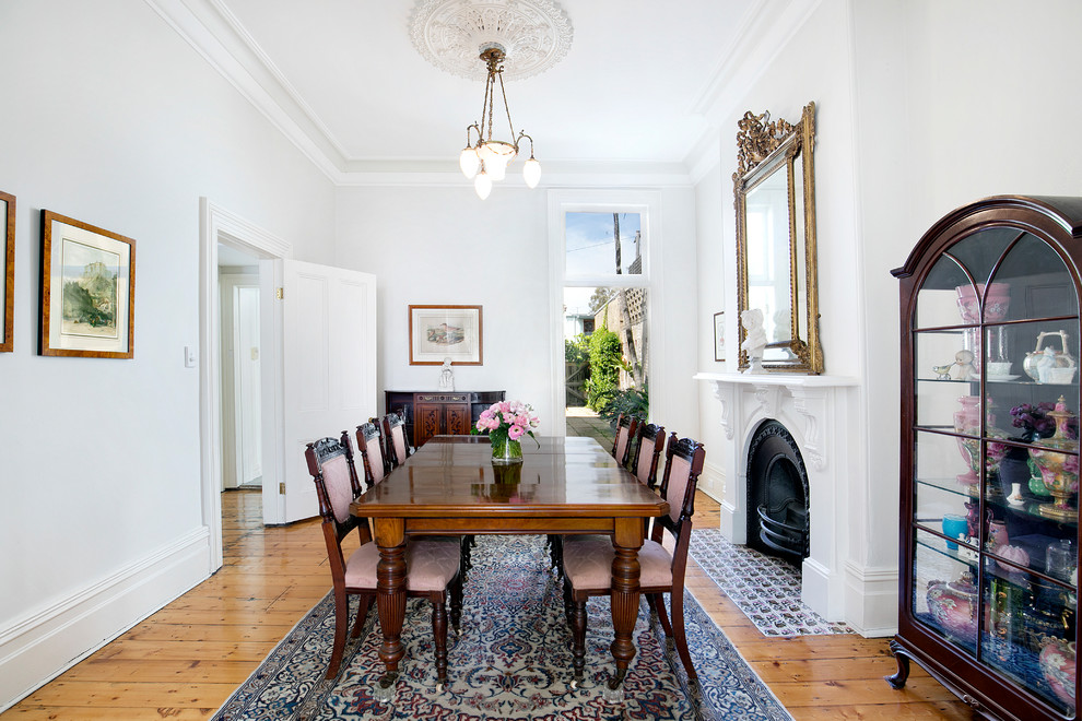 Inspiration for a traditional separate dining room in Sydney with white walls, medium hardwood floors, a standard fireplace, a plaster fireplace surround and brown floor.
