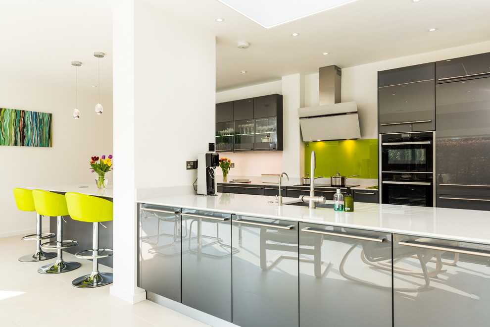 This is an example of a large contemporary galley eat-in kitchen in Hampshire with flat-panel cabinets, grey cabinets, quartzite benchtops, green splashback, glass sheet splashback, porcelain floors, multiple islands, an integrated sink and panelled appliances.