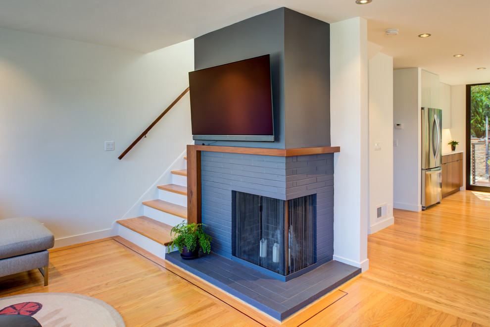 This is an example of a small contemporary open concept living room in San Francisco with white walls, light hardwood floors, a two-sided fireplace, a brick fireplace surround, a wall-mounted tv and beige floor.