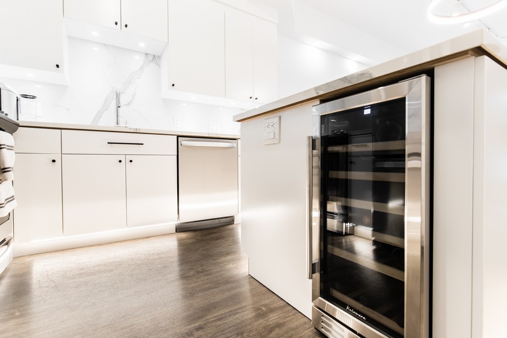 Inspiration for a small modern l-shaped open plan kitchen in Dallas with an undermount sink, flat-panel cabinets, white cabinets, glass benchtops, white splashback, porcelain splashback, stainless steel appliances, vinyl floors, with island, brown floor and white benchtop.