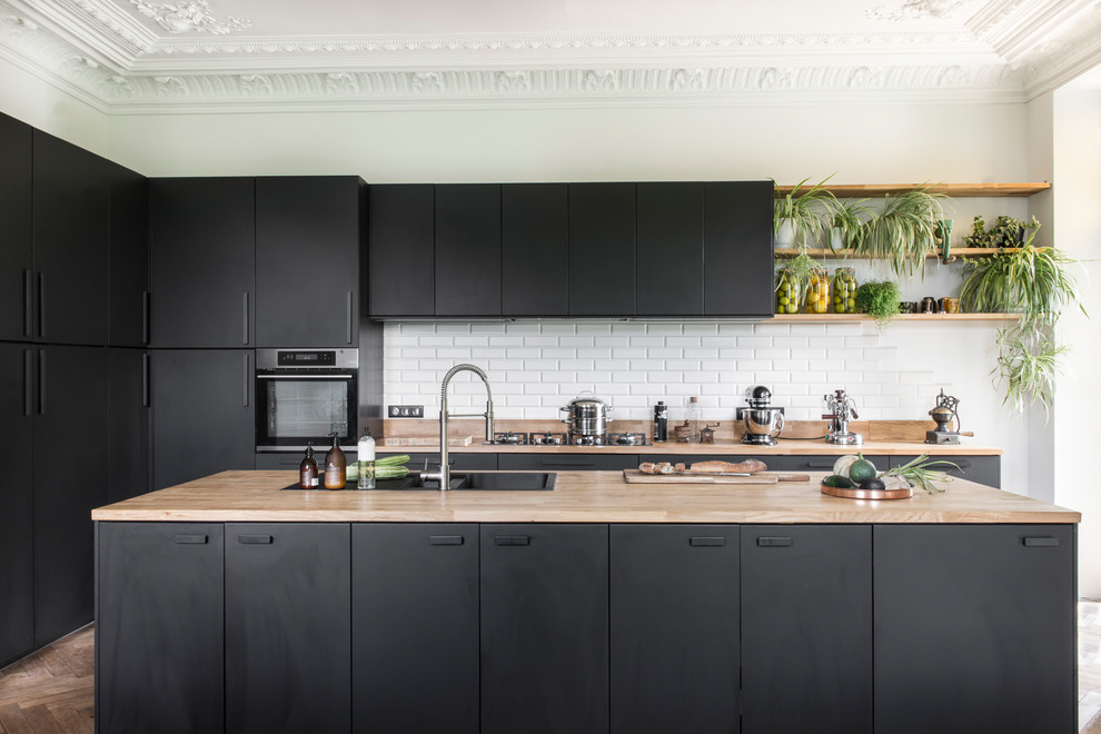 Inspiration for a contemporary l-shaped kitchen in Bordeaux with a drop-in sink, flat-panel cabinets, black cabinets, wood benchtops, white splashback, subway tile splashback, stainless steel appliances, medium hardwood floors, with island, brown floor and beige benchtop.