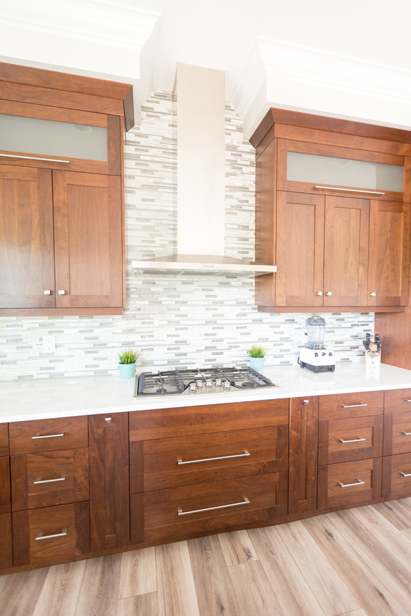 Open concept kitchen - transitional l-shaped beige floor open concept kitchen idea with a farmhouse sink, recessed-panel cabinets, medium tone wood cabinets, gray backsplash, mosaic tile backsplash, stainless steel appliances and an island