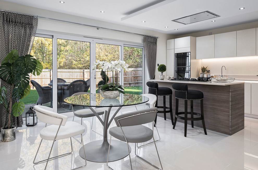 This is an example of a large transitional single-wall eat-in kitchen in Berkshire with flat-panel cabinets, beige cabinets, solid surface benchtops, beige splashback, glass sheet splashback, ceramic floors, with island, grey floor, beige benchtop and black appliances.