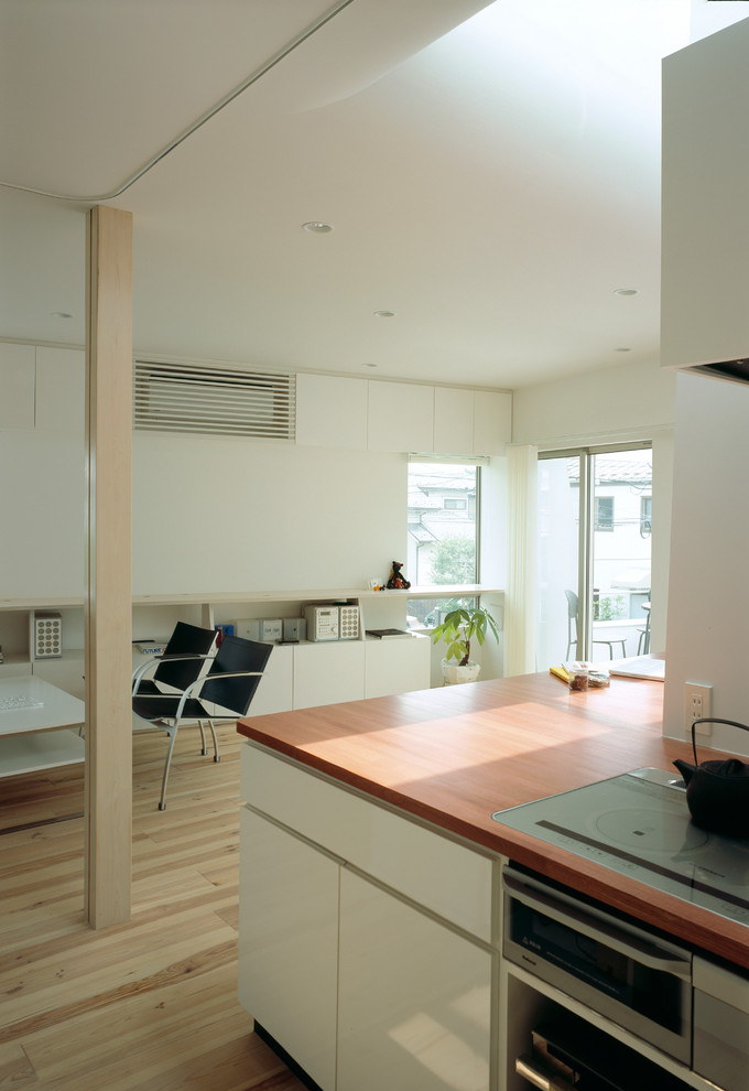 Modern open plan kitchen in Tokyo with beaded inset cabinets, white cabinets, wood benchtops, stainless steel appliances, light hardwood floors, with island, beige floor and red benchtop.