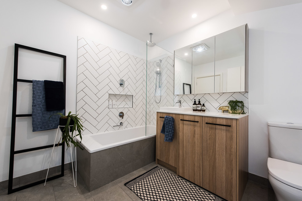 Photo of a mid-sized contemporary master bathroom in Melbourne with flat-panel cabinets, medium wood cabinets, a corner tub, a shower/bathtub combo, a one-piece toilet, white tile, ceramic tile, white walls, porcelain floors, a vessel sink, engineered quartz benchtops, grey floor and an open shower.