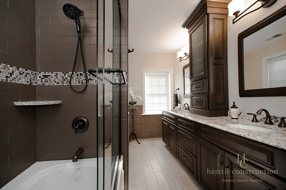 This is an example of a large traditional bathroom in St Louis with raised-panel cabinets, brown cabinets, porcelain tile, an undermount sink, granite benchtops and a shower/bathtub combo.