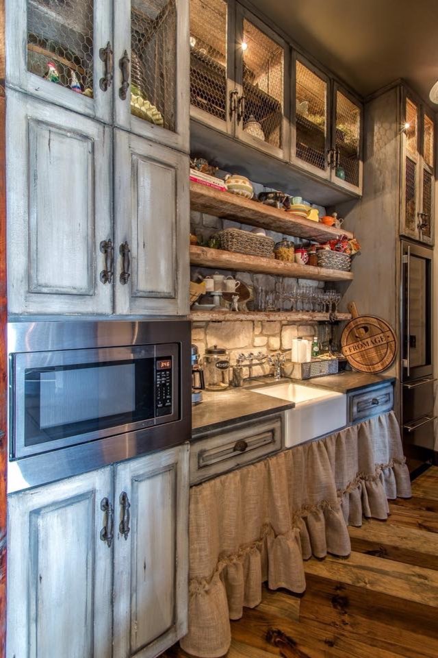 Eat-in kitchen - mid-sized rustic single-wall medium tone wood floor and brown floor eat-in kitchen idea in St Louis with a farmhouse sink, distressed cabinets, gray backsplash, stainless steel appliances, an island, raised-panel cabinets and stone tile backsplash